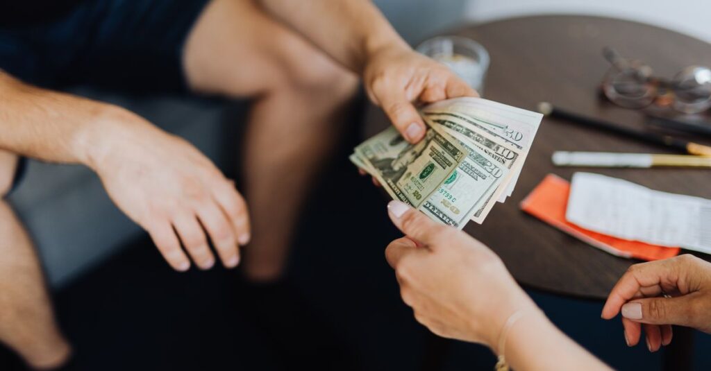 Close-up of hands exchanging US dollar bills, symbolizing a financial transaction or payment.