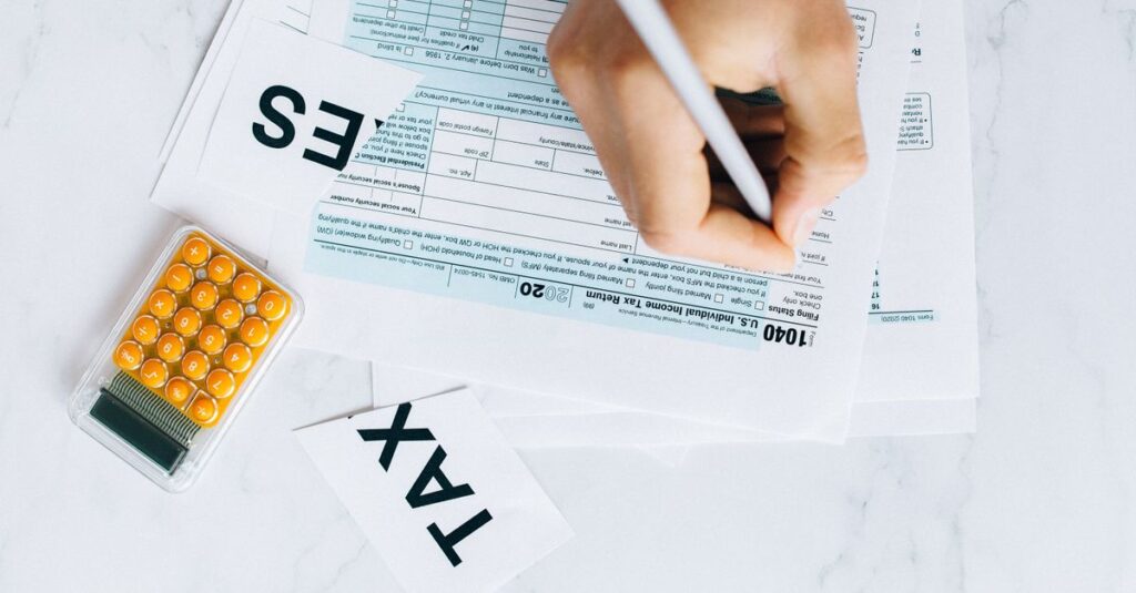 Close-up of hand writing on tax form with calculator nearby on white surface.