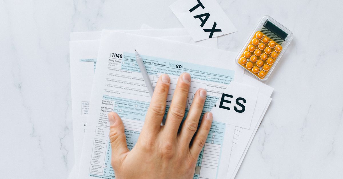 Close-up of a hand on tax form 1040 with a calculator on a desk.