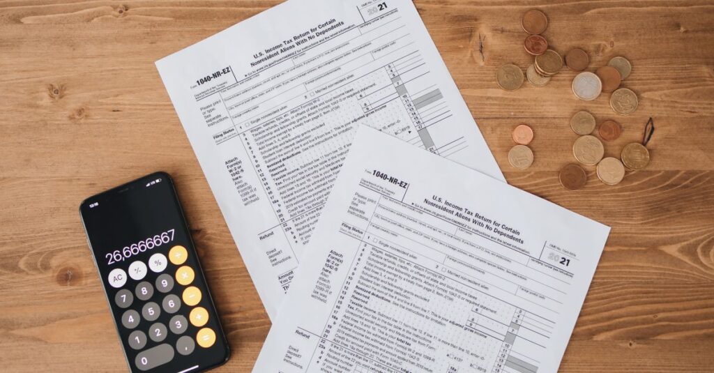 Top view of tax documents, calculator, and coins on wooden table.