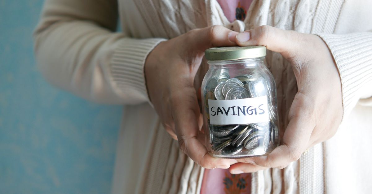 Woman holding a jar labeled 'savings' filled with coins, representing financial savings.