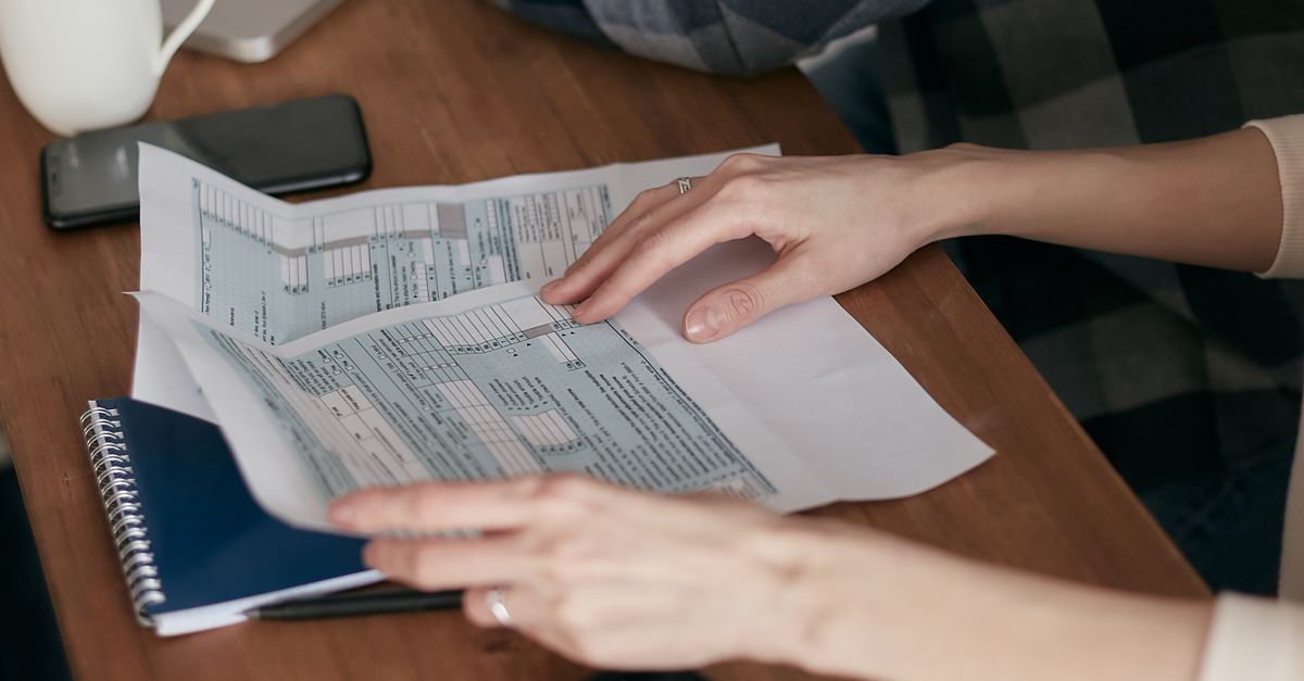 Close-up of hands organizing tax forms on a desk with a calculator, laptop, and notebook.