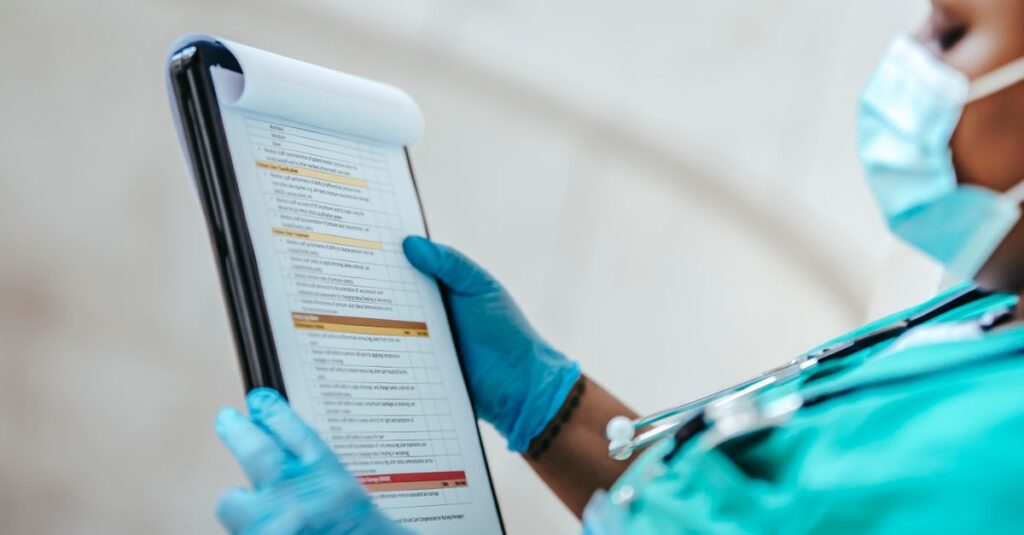 Side view of crop African American female medic in uniform reading text on paper at work