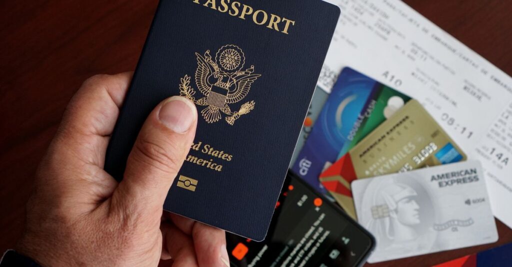 A close-up of a US passport with credit cards, tickets, and a mobile phone on a table.