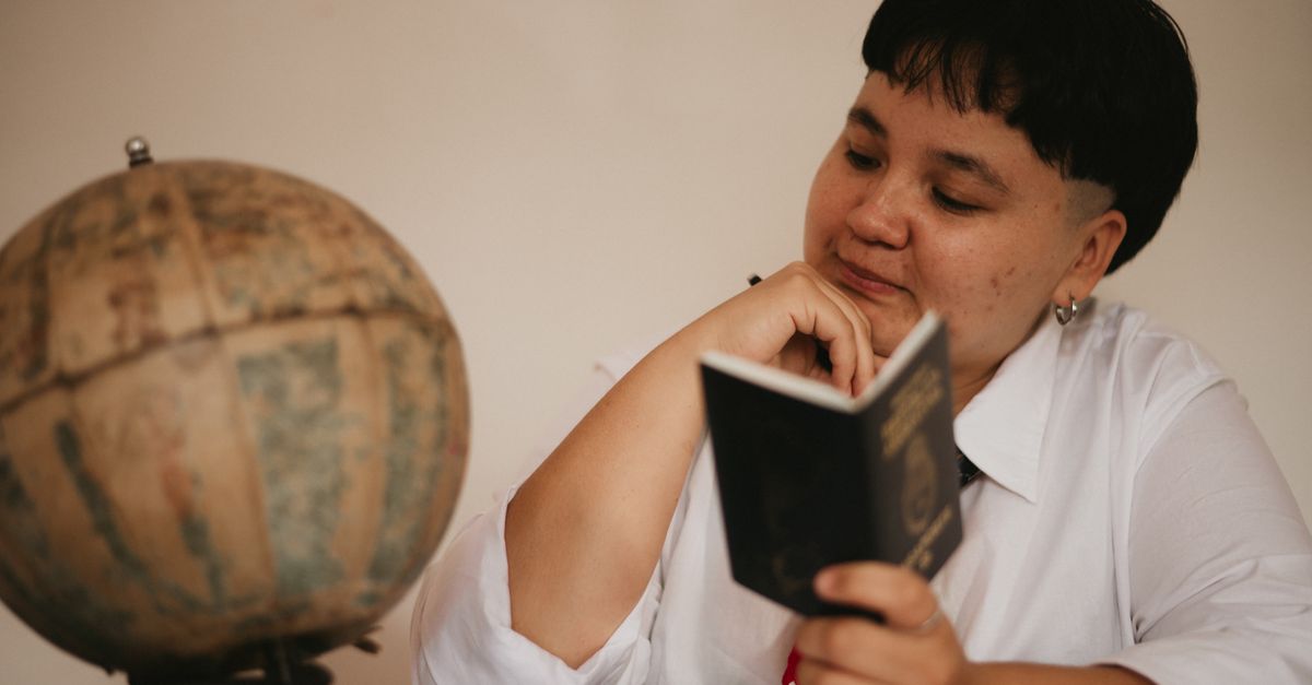 A pensive young adult reading a passport next to a vintage globe, symbolizing travel dreams.