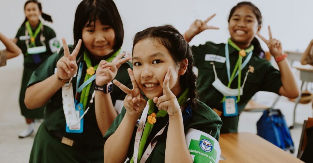 Happy group of Asian Girl Scouts making peace signs in a classroom.