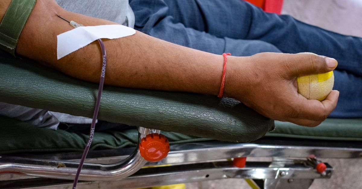 Detail view of a man's arm donating blood in a hospital environment, emphasizing healthcare support.