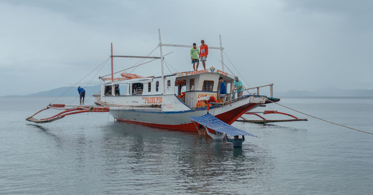 Traditional fishing boat on a serene lake, under an overcast sky with fishermen on board.