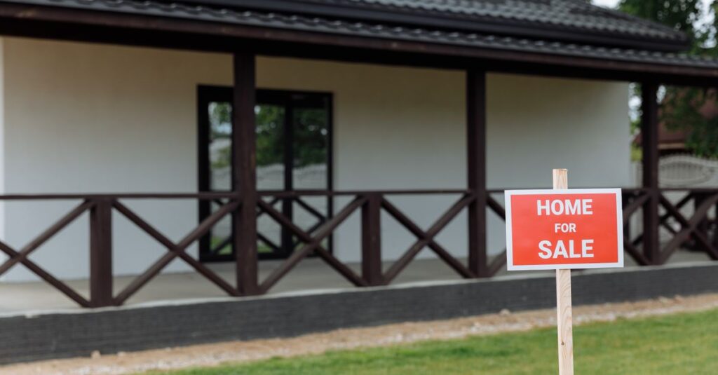 White house with porch and 'Home for Sale' sign on a sunny day.