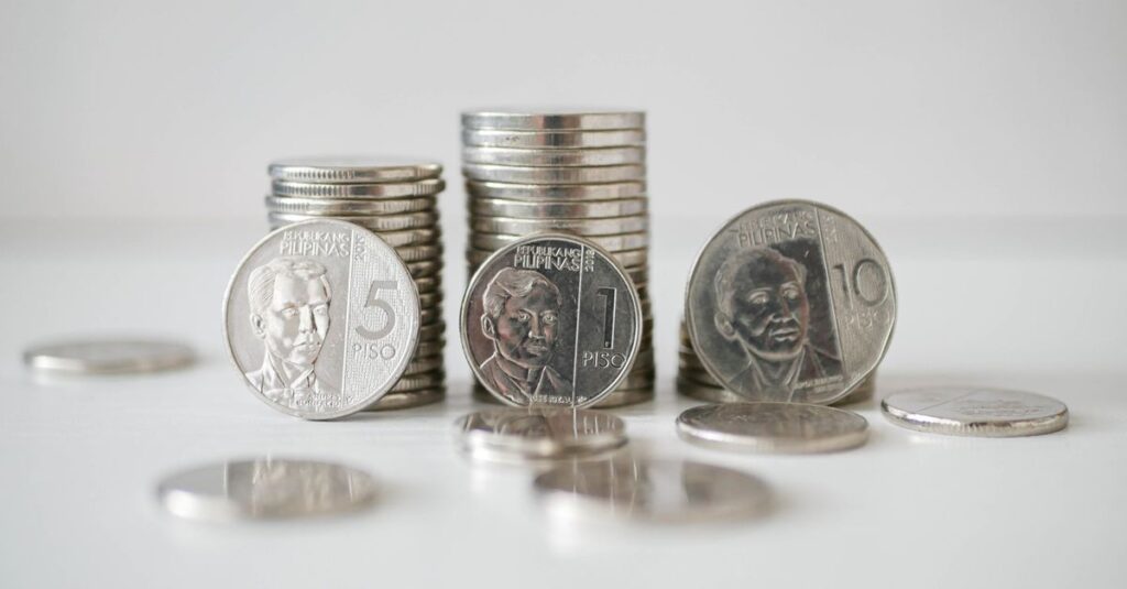 Stacked and scattered Philippine Peso coins in a close-up view on a white surface.