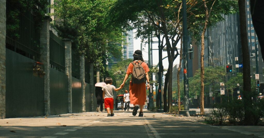 A mother and child stroll hand in hand down a sunny urban street in the Philippines cityscape.