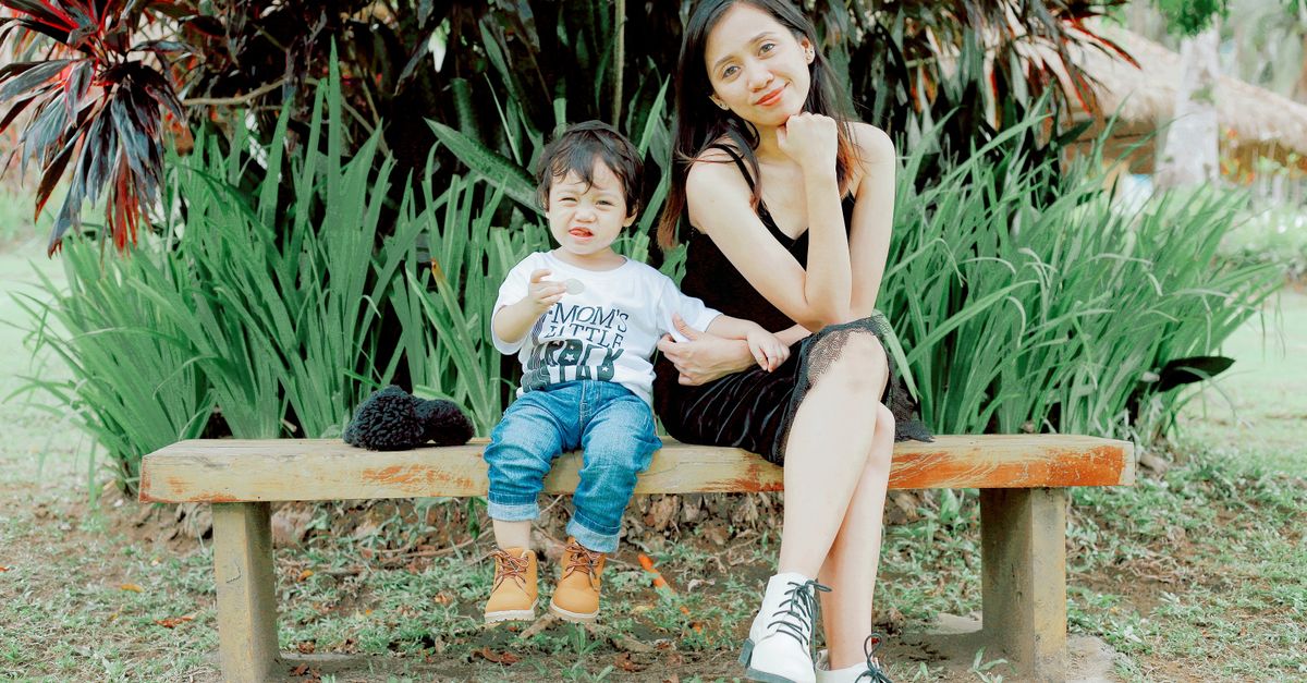 A mother and child sitting together on a bench in a sunny park, Casiguran, Philippines.