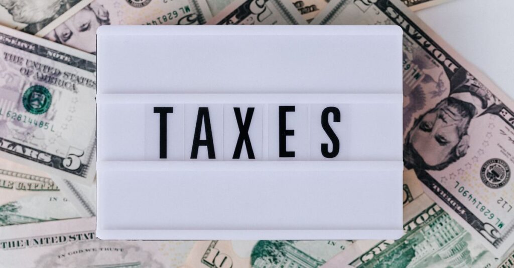 Top view of white vintage light box with TAXES inscription placed on stack of USA dollar bills on white surface
