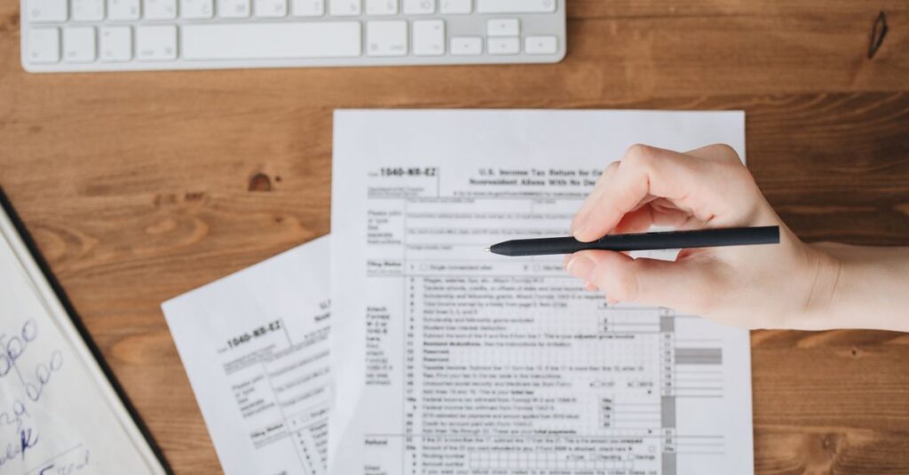 Close-up of a hand holding a pen over US tax forms on a wooden table.