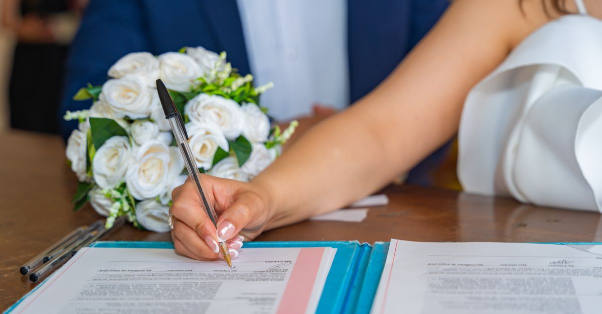 Bride signs marriage certificate during elegant indoor wedding ceremony, symbolizing commitment and togetherness.