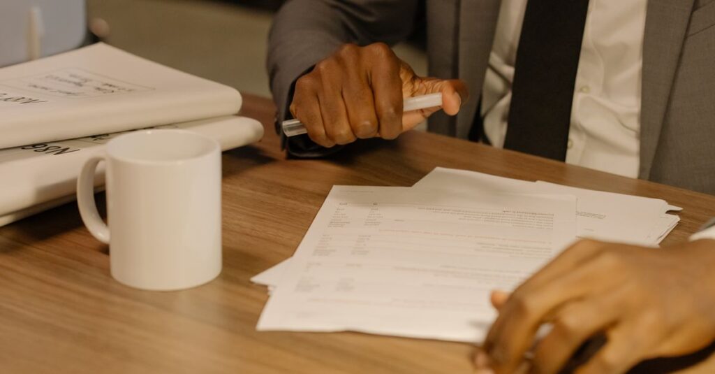 Close-up of a businessman holding and reviewing documents on a wooden desk.